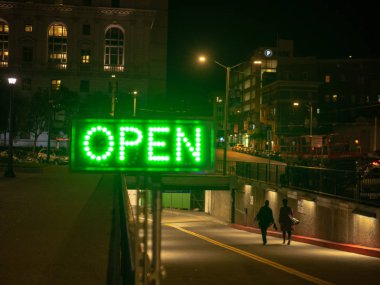 Green lighted open sign in dark city area with people walking in to tunnel clipart