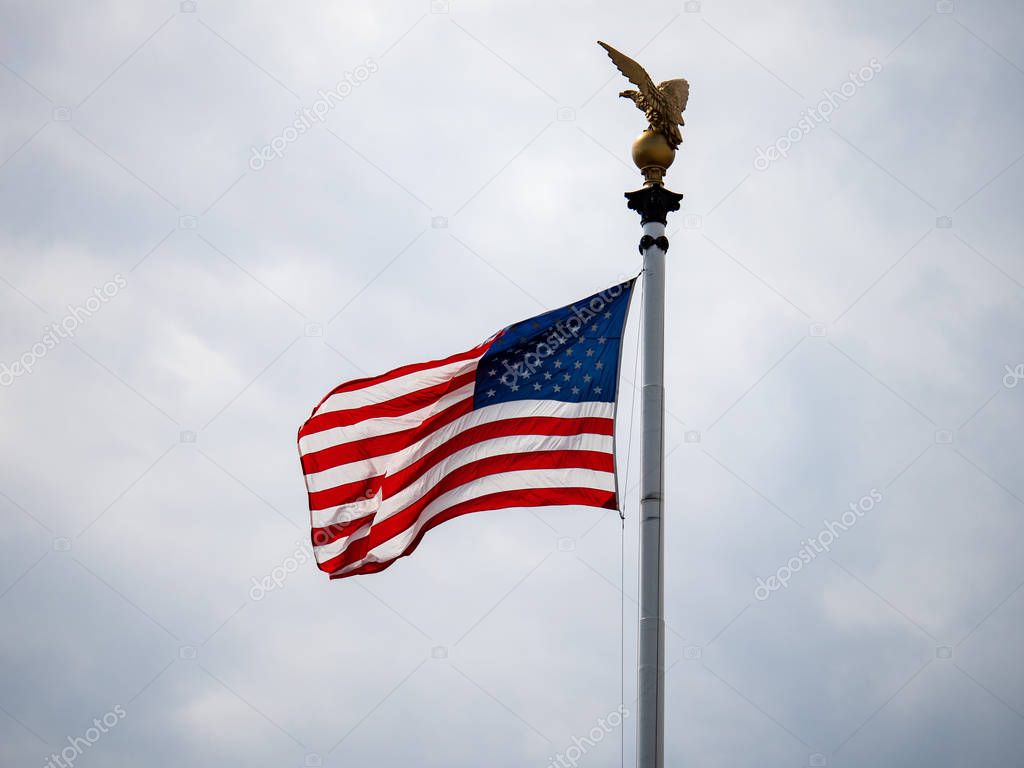 American flag blowing on overcast day with eagle statue over head