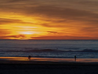 Çiftler, sörfçüler ve aylaklar ile Pasifik Okyanusu üzerinde alacakaranlıkta gün batımı