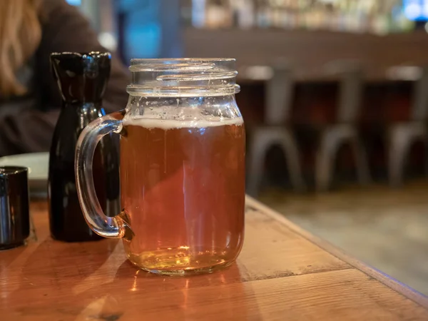 Mason jar mugg med handtag fylld med öl bredvid sake flaska på restaurang — Stockfoto