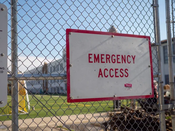 Emergency access sign posted on chain-link fence guarding a school sports area