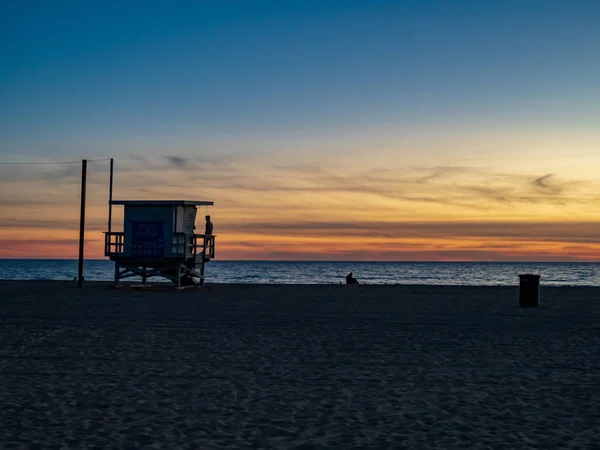 Praia ao pôr do sol crepúsculo com casa de salva-vidas e beachgoers relaxante — Fotografia de Stock