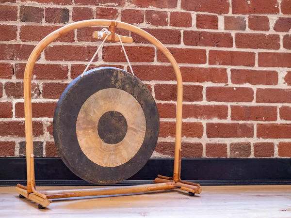 Pequeño gong suspendido sentado en el suelo de madera contra el fondo de la pared de ladrillo — Foto de Stock