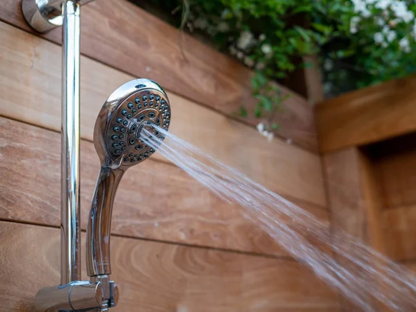 Water steams flowing out of handheld shower head in outdoor shower — Stock Photo, Image