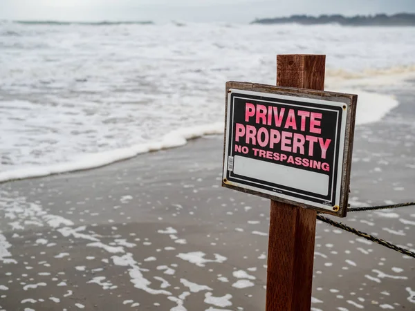 Private property no trespassing sign on pole and wire fence on beach property next to waves — Stock Photo, Image