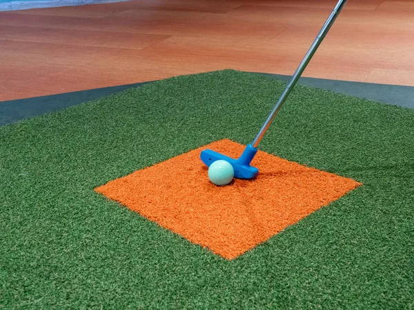 Blue putter on turf lined up next to green golf ball on orange turf on miniature golf course