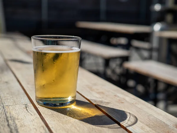 Kort glas blont öl sittande på utomhusbord under sommardagen — Stockfoto