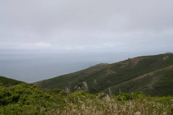 Colina verde na natureza com vista para o grande oceano de água no dia nublado — Fotografia de Stock