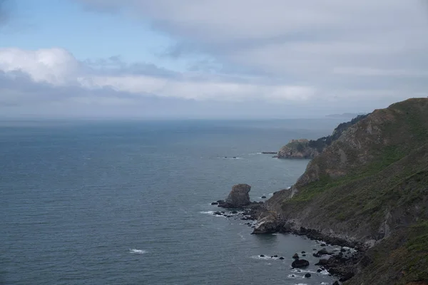 左側に海と曇りの空の海の体を持つ岩の壁の丘側 — ストック写真