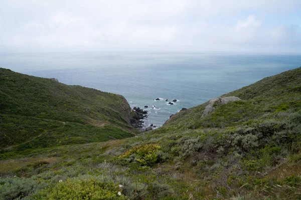 Böljande kullar och vandringsled leder ner i en stenig vik i havet — Stockfoto