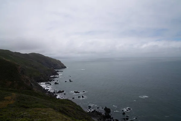 Rotsachtige Zeedijk met bergen en heuvels met Oceaan en wolken naar rechts — Stockfoto