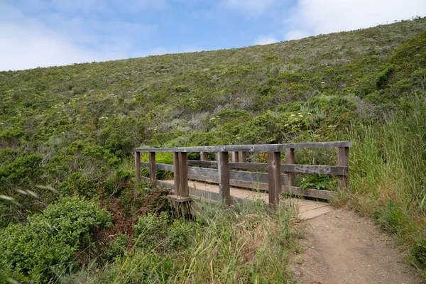 Pequeño puente de madera en camino de tierra por debajo de una gran colina — Foto de Stock