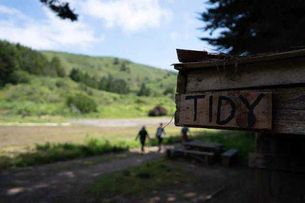 Sign labeled tidy sitting on wooden home on a farm with people walking in background