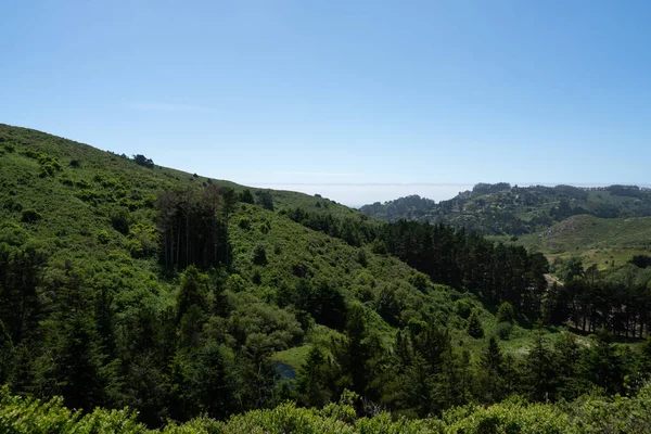 Colinas verdes cénicas, árvores, grama, céu azul claro, habitação residencial à distância — Fotografia de Stock