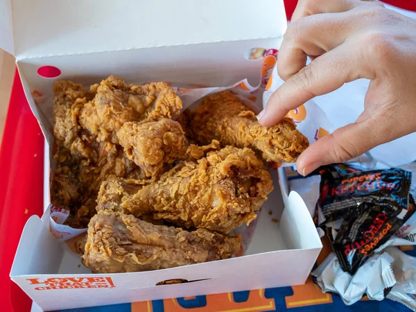 Mujeres mano agarrando pieza de Popeyes Louisiana Pollo de la caja de la cena en el restaurante Imagen De Stock