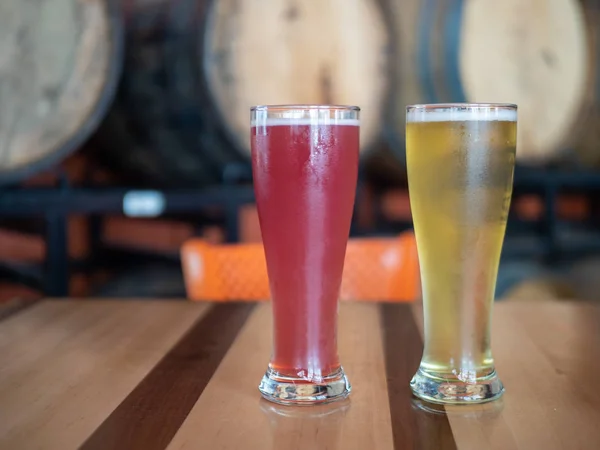 Рожеві і блондинки високі холодні келихи пива на столі перед бочками в пивоварні — стокове фото