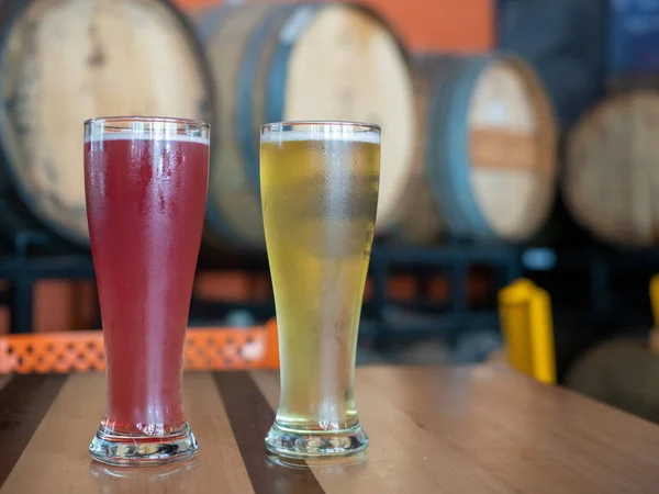 Рожеві і блондинки високі холодні келихи пива на столі перед бочками в пивоварні — стокове фото