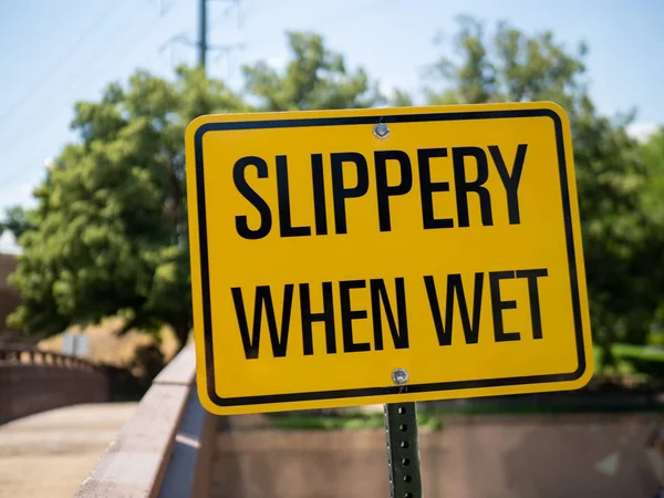 Slippery when wet yellow sign posting outdoors in front of bridge