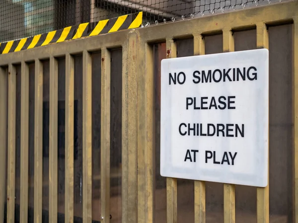 No fumar por favor, los niños en el letrero de juego en la valla en el área de juegos recreativos — Foto de Stock