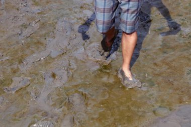 bir adam çamurda yalınayak yürüyor, yerde duran bir adamın ayakları ve çamurda yürümek, çamurlu ıslak ve ayakyürümek, ayak ıslak çamur siyah kil üzerinde yürüyor