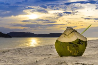 Gün batımında kum plajındaki Hindistan cevizi kokteyl