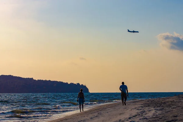 Силует пари на пляжі на фоні неба заходу сонця з літаком під час посадки — стокове фото