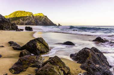 Gün doğumunda kumlu plajda kayalar ve taşlar, Portekiz.