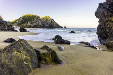 Kumlu plajda okyanus dalgası ve kayalıklar, Portekiz