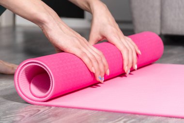 Oturma odasında spor yaptıktan sonra yoga ya da spor salonu paspası katlayan çekici genç bir kadın. Sağlıklı yaşam, sağlıklı kavramları koru.