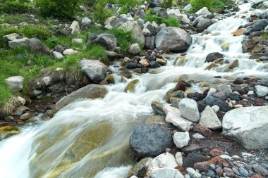 Bir dağ şelalesinin dibindeki kayaların üzerinden sular akar. Güzel dağ nehri