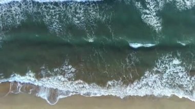 Kumlu sahil şeridinde deniz dalgaları dalgalanırken güzel görüntülerin drone üst görüntüsü