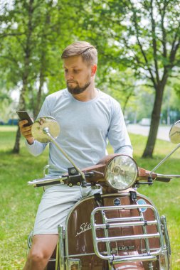 parkta vintage bir scooter sürme telefon ile genç adam