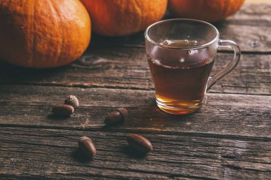 Şükran veya halloween kavramı bir pumpkins, bir cam bardak çay ve meşe palamutları ahşap bir tablo için sonbahar arka plan