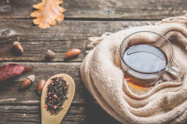 Sonbahar kompozisyon, sonbahar yaprakları, meşe palamutları, cam bardak çay ve eski ahşap masa arka plan üzerinde sıcak bir eşarp.