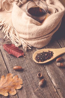 Sonbahar kompozisyon, sonbahar yaprakları, meşe palamutları, cam bardak çay ve eski ahşap masa arka plan üzerinde sıcak bir eşarp.