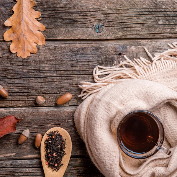 Sonbahar kompozisyon, sonbahar yaprakları, meşe palamutları, cam bardak çay ve eski ahşap masa arka plan üzerinde sıcak bir eşarp.