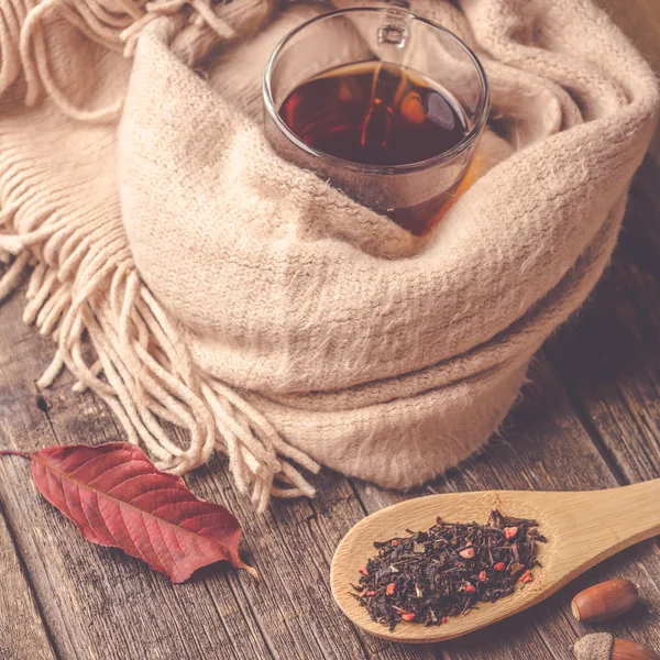 Sonbahar kompozisyon, sonbahar yaprakları, meşe palamutları, cam bardak çay ve eski ahşap masa arka plan üzerinde sıcak bir eşarp.