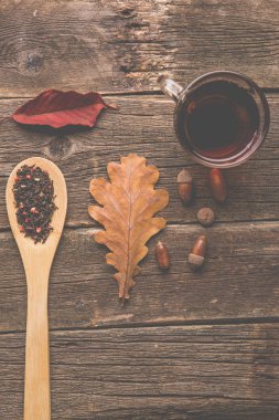 Sonbahar ile çay yaprakları, meşe palamudu ve ahşap masa kaşık kuru bitkisel çay. Tonda fotoğraf