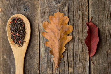 Sonbahar ile çay yaprakları, meşe palamudu ve ahşap masa kaşık kuru bitkisel çay. Tonda fotoğraf