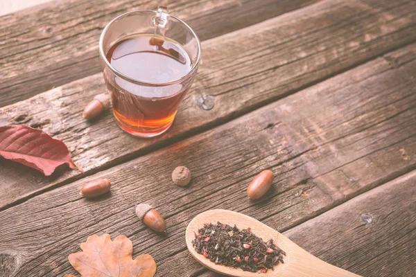 Sonbahar ile çay yaprakları, meşe palamudu ve ahşap masa kaşık kuru bitkisel çay. Tonda fotoğraf