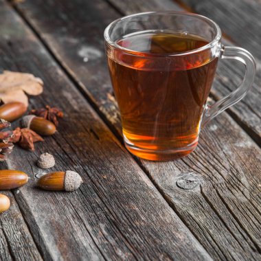 Ahşap bir tabloda çay, meşe yaprağı, çam kozalakları ve meşe palamudu bir cam bardak ile sonbahar arka plan kavramı