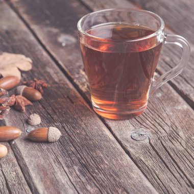 Ahşap bir tabloda çay, meşe yaprağı, çam kozalakları ve meşe palamudu bir cam bardak ile sonbahar arka plan kavramı