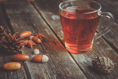 Ahşap bir tabloda çay, meşe yaprağı, çam kozalakları ve meşe palamudu bir cam bardak ile sonbahar arka plan kavramı