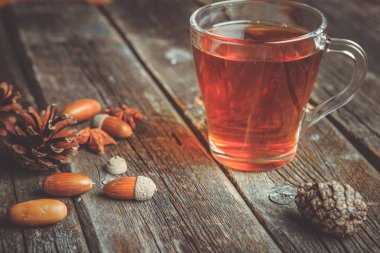 Ahşap bir tabloda çay, meşe yaprağı, çam kozalakları ve meşe palamudu bir cam bardak ile sonbahar arka plan kavramı