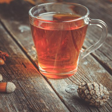 Ahşap bir tabloda çay, meşe yaprağı, çam kozalakları ve meşe palamudu bir cam bardak ile sonbahar arka plan kavramı