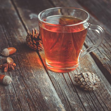 Ahşap bir tabloda çay, meşe yaprağı, çam kozalakları ve meşe palamudu bir cam bardak ile sonbahar arka plan kavramı
