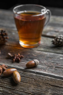 Ahşap bir tabloda çay, meşe yaprağı, çam kozalakları ve meşe palamudu bir cam bardak ile sonbahar arka plan kavramı