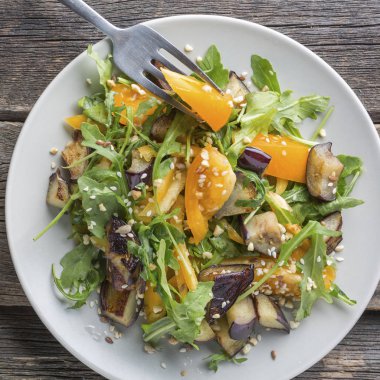 Sebze - domates, roka, sağlıklı salata ızgara patlıcan ve tohum bir plaka üzerinde. Vegan gıda.