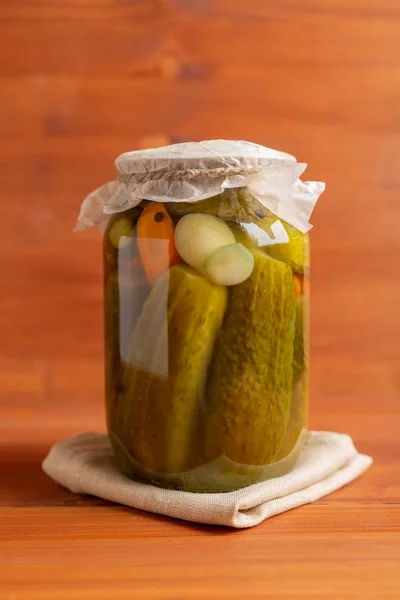 Glass jar with pickled cucumbers on brown wooden background — Stock Photo, Image