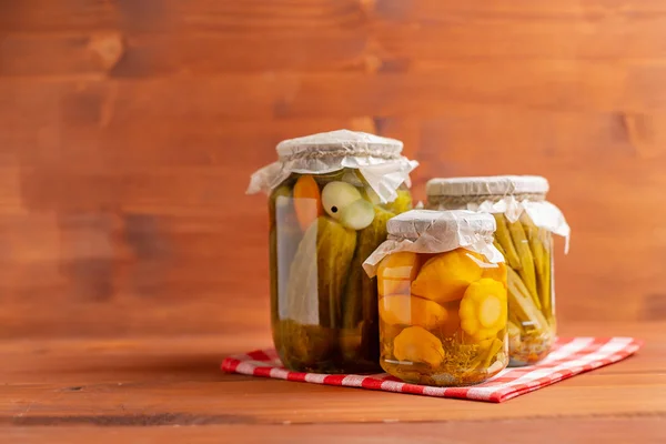 Jars of pickled vegetables: cucumbers, tomatoes, okra, eggplants on rustic wooden background. — Stock Photo, Image